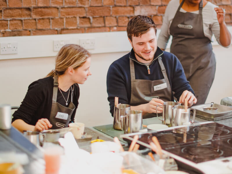 A couple melt wax in silver jugs as they learn how to make candles. 